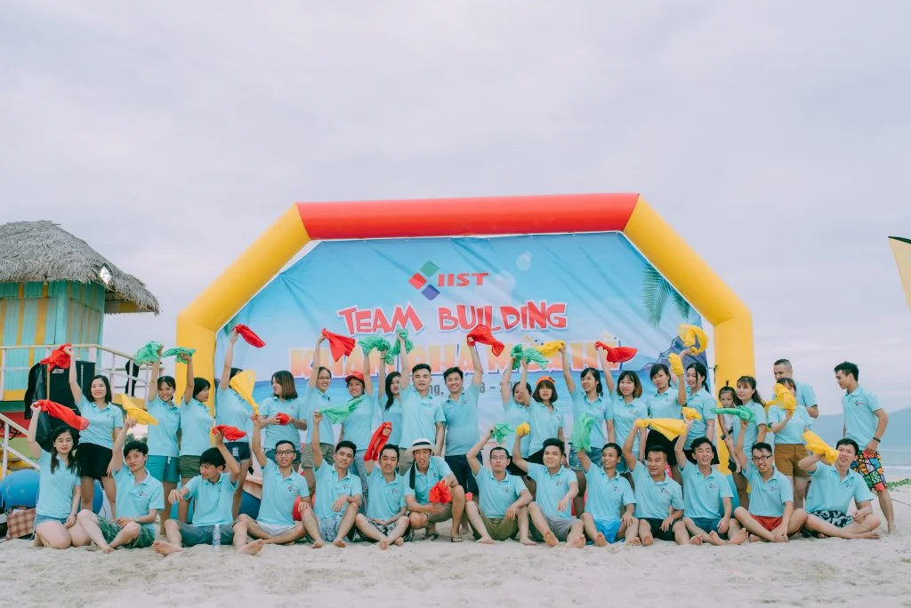 Ảnh hoạt động team building bãi biển với áo chia đội màu xanh nổi bật, phù hợp minh họa cho phần tư vấn đồng phục theo màu team.